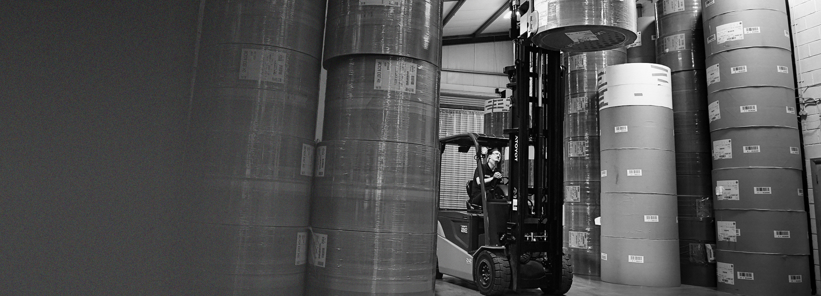 Production worker in a warehouse using a forklift to move large reels of printing paper