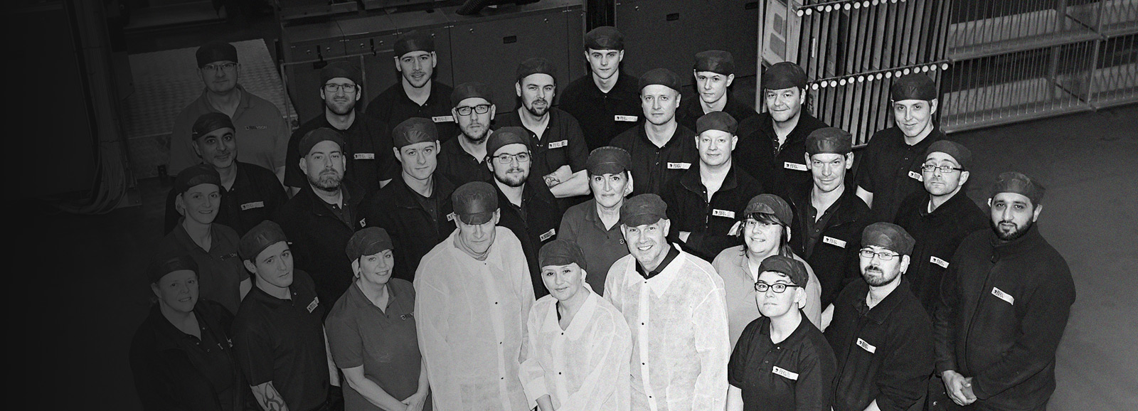 Large group of production employees stood together smiling at camera